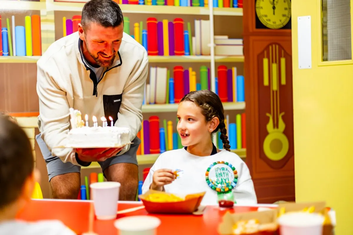 A dad bringing out the birthday cake at a Happy Town party